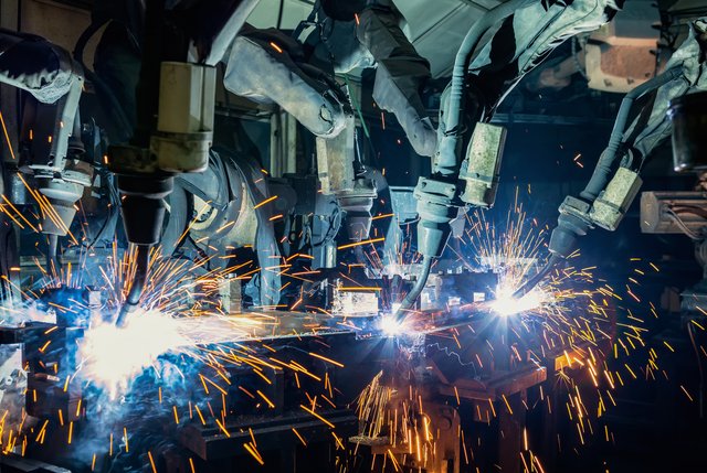Mehrere Industrieroboter schweißen Metallbauteile in einer Produktionshalle, Funken fliegen